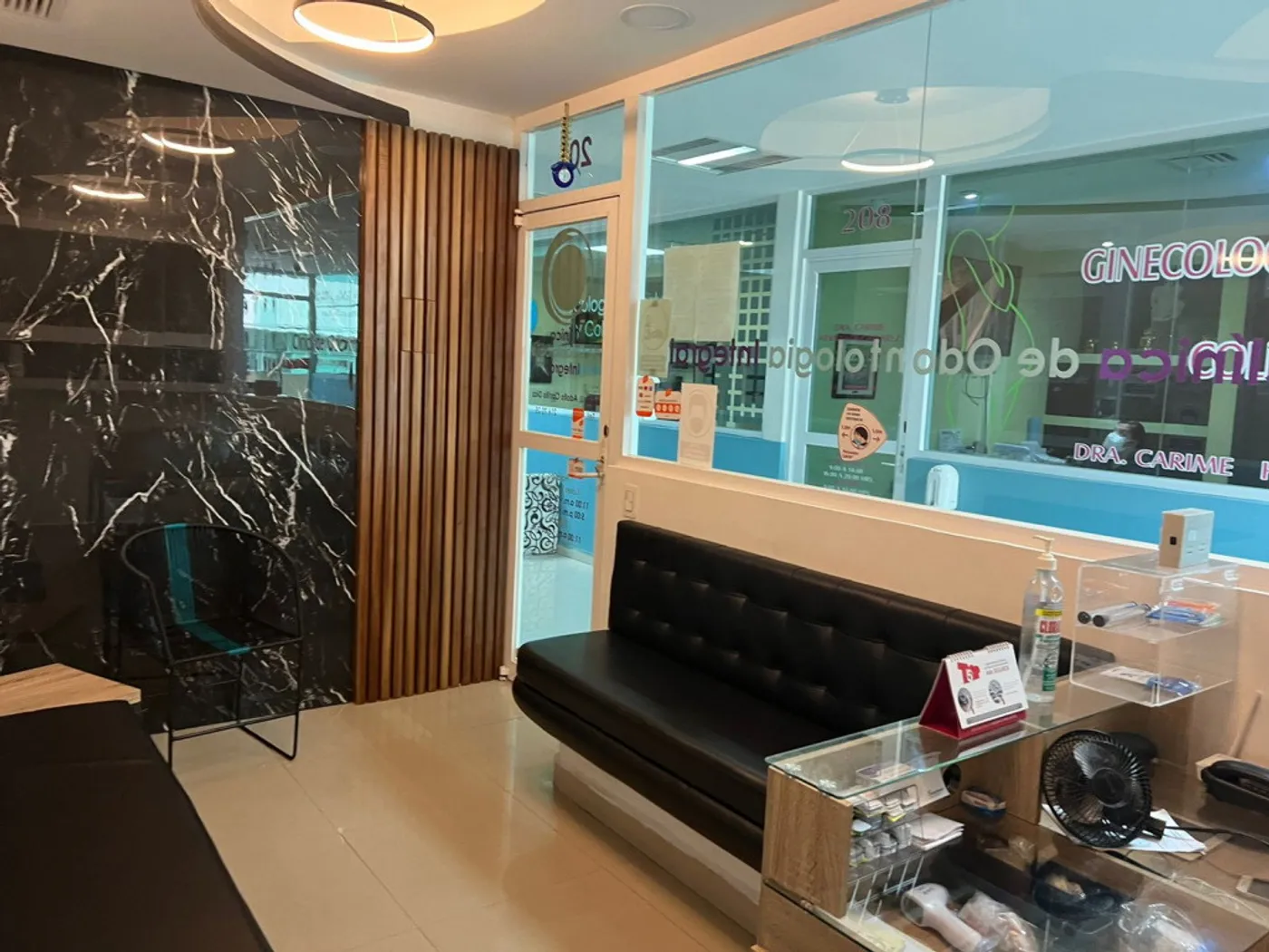 Área de recepción con sillones negros, muro de mármol oscuro y vidrio hacia el consultorio